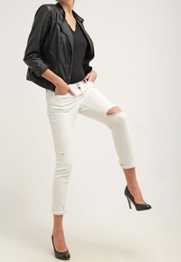 Svart läderjacka, figursydd svart topp, vita söndriga skinny jeans och svarta högklackade skor. Outfiten är avslappnad med en modern stil.