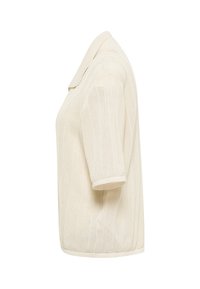 Kurzärmeliges Poloshirt aus Strick in Cremefarbe mit einem strukturierten Zickzackmuster und einem umgeschlagenen Kragen, von der Seite vor weißem Hintergrund gezeigt.