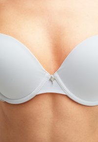 Lichtgrijze gewatteerde beha met een gladde oppervlakte, onderwire ondersteuning, kantafwerking en een zilveren decoratieve accent in het midden.