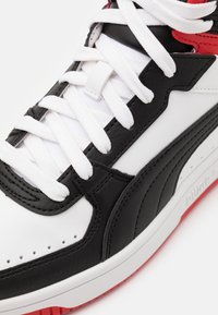 Sport sneakers met een zwarte leren bovenkant, witte mesh tong en veters, rode accenten en een gestructureerde witte zool met een rode onderkant.
