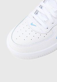 Pantof sport din piele albă cu suprafață texturată, accente bleu deschis, vârf perforat și talpă din cauciuc albă.