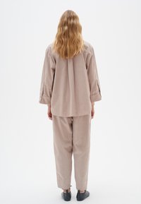 Løs pasform beige corduroy skjorte og bukser sæt med lange ærmer, knapdetaljer og ankellange kanter. Sorte sko fuldender outfittet.