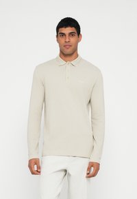 Polo bege de manga comprida com gola, abertura de três botões e detalhe subtil do logótipo no peito. Textura suave e corte regular.