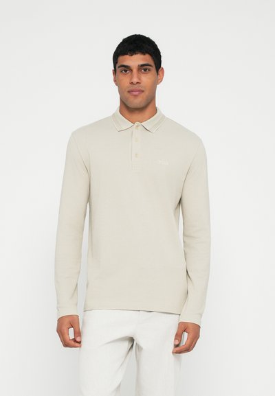 Polo à manches longues beige avec col, patte de boutonnage à trois boutons et détail de logo subtil sur la poitrine. Texture lisse et coupe régulière.