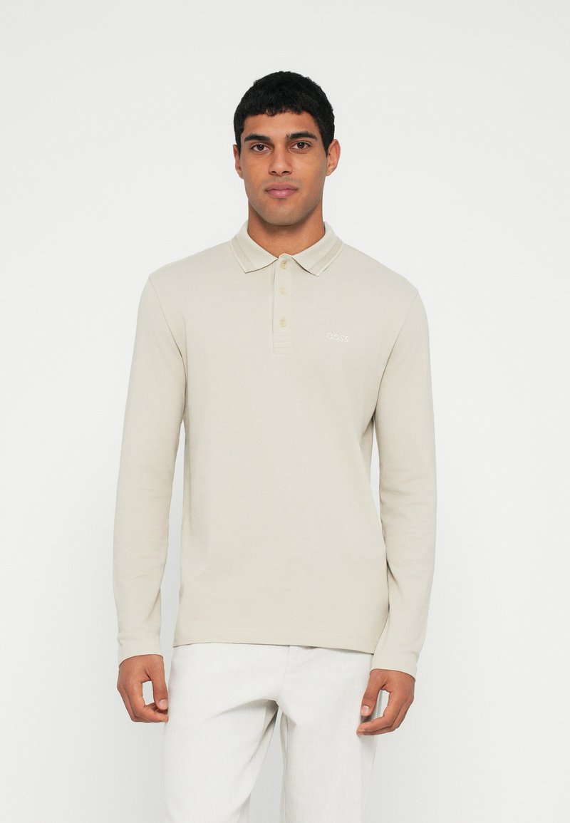 Polo bege de manga comprida com gola, abertura de três botões e detalhe subtil do logótipo no peito. Textura suave e corte regular.