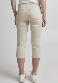 Beżowe spodnie 3/4 wykonane z elastycznego materiału, z dwiema tylnymi kieszeniami i dopasowanym krojem, w zestawie z białymi trampkami.