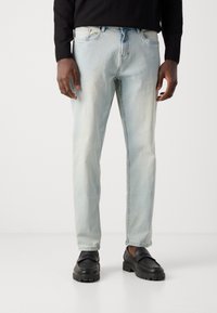 Light blue denim jeans with a straight cut, featuring a faded finish and five-pocket design. Paired with black loafers for contrast.