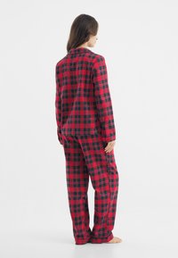 Conjunto de pijama de cuadros rojos y negros compuesto por una camisa abotonada y pantalones de corte holgado, fabricado en una tela suave, con cuello estándar y mangas largas.
