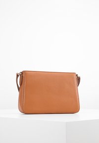 Vaaleanruskea nahkainen olkalaukku suorakulmaisella muotoilulla, sileällä pinnalla ja hopeisilla metalliosilla kiinnitetty hihna. Minimalistinen muotoilu.