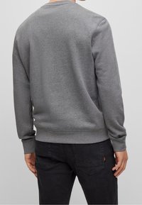 Felpa grigia con scollo rotondo, polsini e orlo a costine, realizzata in materiale morbido. Caratterizzata da una texture liscia e un design casual.