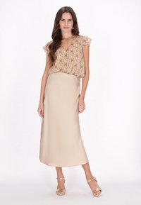 Bluse med blomsterprint i blød pink med voluminøse ærmer, parret med en lang, beige satin nederdel og metallic stropstiletter.