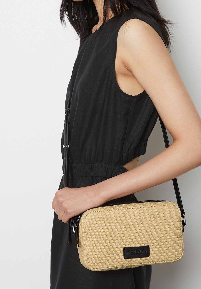 Bolso cruzado de paja tejida con forma rectangular, color beige natural, cierre de cremallera negro y un acento de piel con un logotipo.