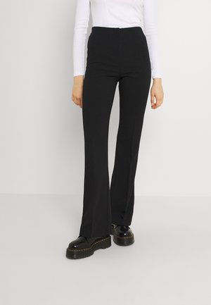 Person wearing black high-waist flared pants, black platform shoes, and a fitted long-sleeve white top on a plain background.