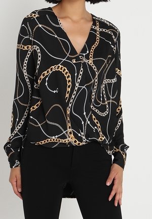 Black long-sleeve blouse with gold and white chain patterns, worn with black pants on a person standing against a plain background.
