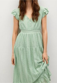 Robe midi vert clair avec des manches courtes à volants, boutons sur le devant et motifs géométriques texturés. Design fluide avec une taille cintrée.