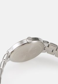 Orologio in acciaio inossidabile argento con cassa rotonda, corona testurizzata e bracciale a maglie flessibili. Superficie liscia con un design minimalista.