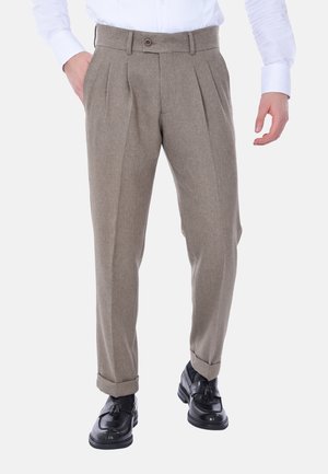 Pantaloni beige a pieghe con vestibilità su misura e orli arrotolati, realizzati in tessuto testurizzato. Abbinati a mocassini neri.