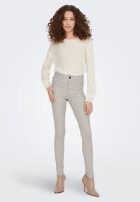 Beige hoge taille skinny jeans met een textuur gebreide crèmekleurige trui, gecombineerd met lichtbeige haklaarsjes tot de enkel. Eenvoudig en aansluitend ontwerp.