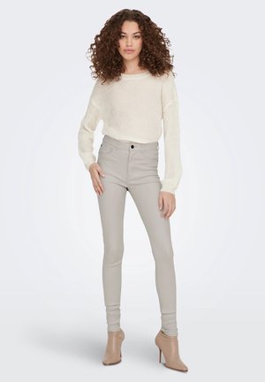Jean skinny taille haute beige accompagnés d'un pull en maille crème texturé, associés à des bottines à talons beige clair. Conception simple et ajustée.