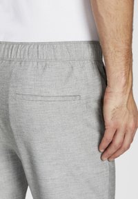 Pantalon en mélange de lin gris avec une taille élastique, présentant une texture subtile et une seule poche arrière à ouverture étroite.