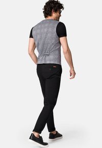 Szary kamizelka w kratkę z zapięciem na plecach, noszona na czarnym t-shircie, w połączeniu z czarnymi spodniami i czarnymi sneakersami o fakturze.