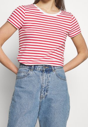 Femme portant un t-shirt à manches courtes rayé horizontal rouge et blanc, rentrée dans un jean bleu clair taille haute, les mains posées sur les hanches.