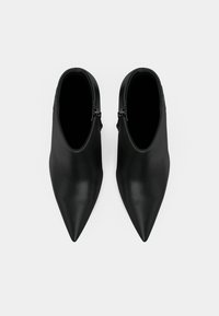 Botas negras de tobillo con punta afilada y textura de cuero suave, que cuentan con un cierre de cremallera lateral y un diseño elegante y afilado.