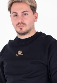 Czarna bluza z okrągłym dekoltem, z złotym logo "Aquascutum ACTIVE" na klatce piersiowej. Miękka tkanina o gładkiej strukturze.