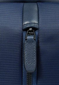 Bolsa de tela azul marino con superficie texturizada, que cuenta con una cremallera negra y una lengüeta de cuero para facilitar la apertura y el cierre.