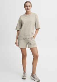 Beige t-shirt i bomullsblandning i oversize, parat med matchande shorts, har avslappnad passform, rund halsringning och sidofickor. Avslappnat fotbeklädnad ingår.