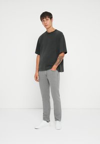 Camiseta de gran tamaño gris oscuro, de mangas cortas, combinada con jeans ajustados gris claro. Zapatillas blancas completan el atuendo. Diseño simple y casual.