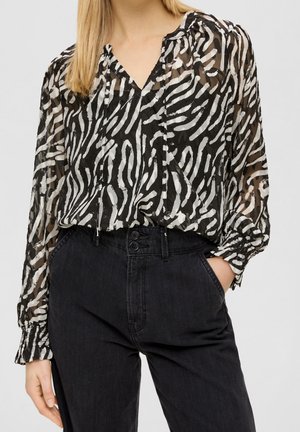 Blouse à imprimé zèbre noir et blanc avec des manches longues, un col en V et des poignets froncés, associée à un jean en denim noir taille haute avec des boutons décoratifs.