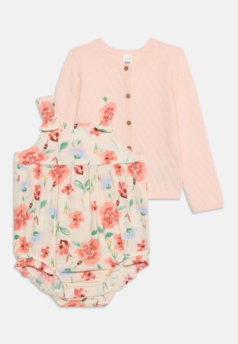 Cardigan tricoté rose pour bébé avec boutons en bois, associé à une grenouillère sans manches à motifs floraux avec des fleurs roses et bleues et des bretelles à volants.