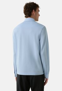 Lichtblauwe langlopende shirt met een kraag, knoopmanchetten en een gladde textuur. Eenvoudig ontwerp met een ontspannen pasvorm.