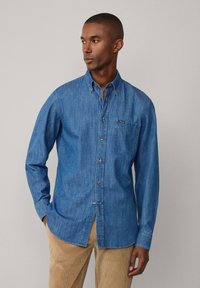 Denim overhemd in medium blauw, met knoopsluiting en een kraag, enkele borstzak en subtiele stikdetails. Lange mouwen met knoopmanchetten.