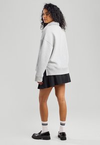 Harmaa ylipitkä collegepaita korkealla kauluksella, yhdistettynä laskostettuun mustaan hameeseen, polven yli ulottuviin sukkiin ja mustiin paksupohjaisiin kenkiin.