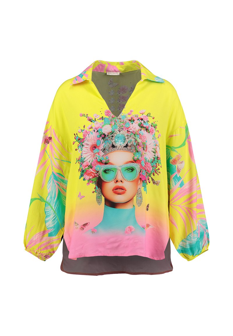 Gelbe Bluse mit einem grafischen Blumen-Gesichtsdruck, der leuchtend pinke und türkisfarbene Akzente enthält, einem V-Ausschnitt und langen Ärmeln.