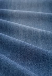 Denim tkanina u različitim nijansama plave boje, koja prikazuje glatku teksturu i presavijen dizajn s suptilnim sjenčanjima i tkanim uzorcima.