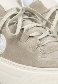 Beżowe zamszowe sneakersy z kremowymi sznurówkami i gumową podeszwą. Posiadają okrągłe logo z boku oraz obszycia wzdłuż krawędzi.