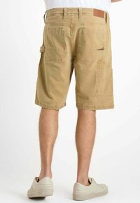 Shorts cargo en coton brun clair avec plusieurs poches, des détails cousus et un petit écusson logo sur la ceinture.