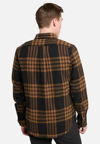 Camicia a flanella a quadri nera e arancione con maniche lunghe e yoke posteriore dritto. La trama del tessuto appare morbida con un classico motivo a quadri.