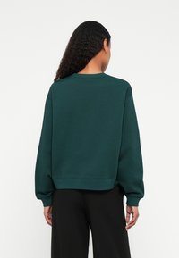 Felpa verde sovradimensionata con scollo rotondo, polsini e orlo a costine. Texture liscia, design casual e cuciture delle spalle scese.