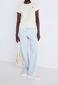 Jasnożółty t-shirt w paski, jasnoniebieskie szerokie dżinsy oraz różowe trampki w wzory. Dodatek: kremowa torebka z szydełkowym wzorem i żółtymi kwiatami.