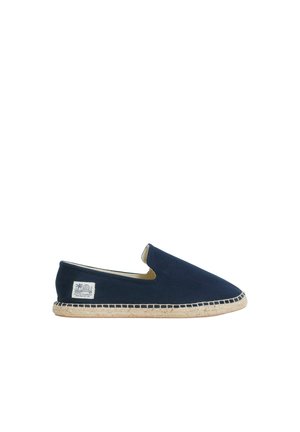 Dunkelblaue Slip-on-Espadrille mit natürlicher Jutesohle und kleinem weißen Stofflabel an der Außenseite nahe der Ferse.