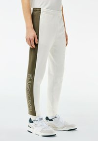 Bela in olivno zelena bombažna trenirka z elastiko v pasu, na strani z velikim logotipom "LACOSTE". Mehka tekstura.