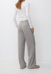 Pantalons larges gris clair avec une texture lisse, dotés d'une seule poche arrière, associés à un haut à manches longues ajusté en côtes blanches.