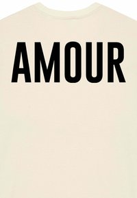 Kreminės spalvos marškinėliai su ryškiu juodu užrašu "AMOUR" nugaros pusėje. Pagaminti iš medvilnės, jie turi apykaklę ir trumpas rankoves.