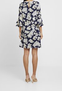 Blommig klänning i marinblått med vita och gula blommor. Har volang ärmar och en nyckelhålsdesign på baksidan. Slät tygtextur.