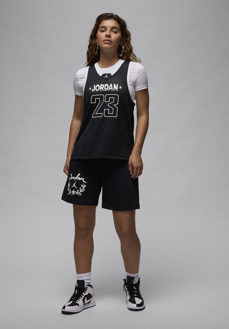Schwarzes Mesh-Trikot mit "JORDAN" und "23" in Weiß, kombiniert mit schwarzen Shorts mit weißem Blattdesign. Getragen mit schwarz-weißen Turnschuhen.