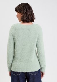 Hellgrüner, flauschiger Pullover mit rundem Halsausschnitt und langen Ärmeln. Sanfte Textur, lockere Passform und gerippte Bündchen und Saum.